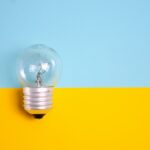 A close-up of a clear light bulb against a vibrant yellow and blue background, symbolizing innovative ideas in smart home technology with HomeWizard.