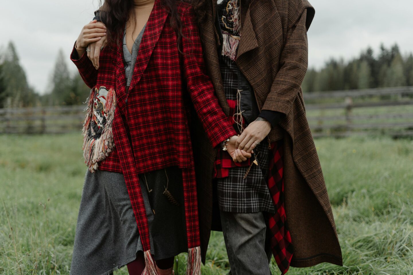 A couple in plaid Woolrich coats stands hand in hand in a field, showcasing the timeless appeal of heritage-inspired outdoor wear.